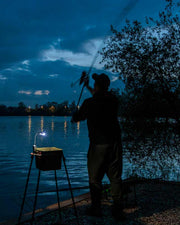 Person fishing at night by a lake with a light on a stand.