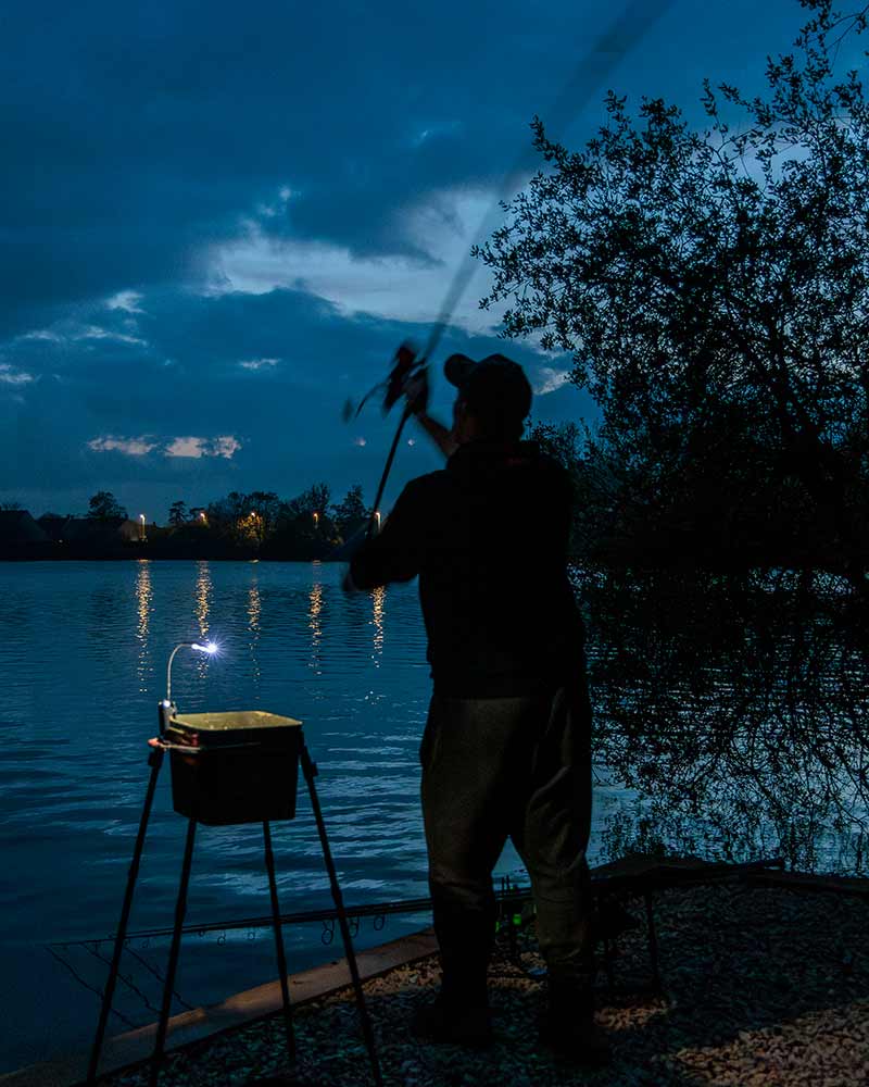 Person fishing at night by a lake with a light on a stand.